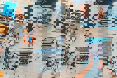 Several laptops and phones on a busy desk